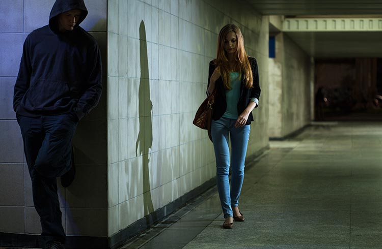 A woman walking through a dim tunnel with a man in a hoodie behind her