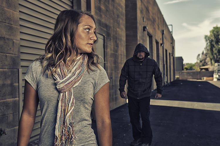 A woman walking away from a man in a hooded jacket in an alley